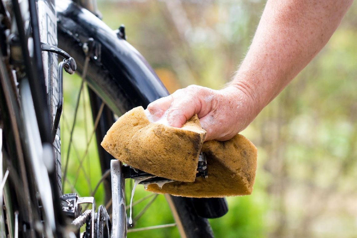 Hand hält Schwamm und reinigt Fahrrad